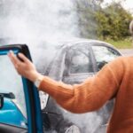 A woman in an orange sweater gets out of a car after it collided with another vehicle. She is rubbing the back of her neck.