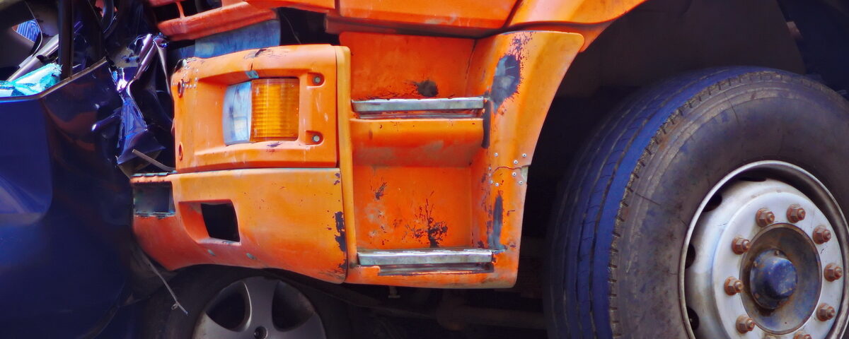 A close-up of an orange truck that has rear-ended a blue passenger car. The back end of the blue car is completely crumpled.