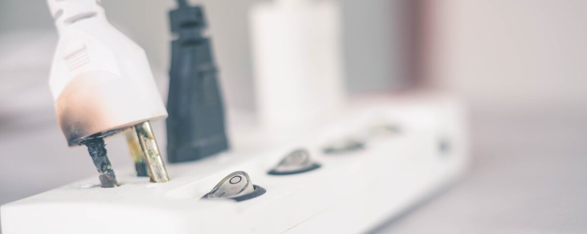A power strip with three cables plugged into it. The plug in the foreground is noticeably damaged and burnt.