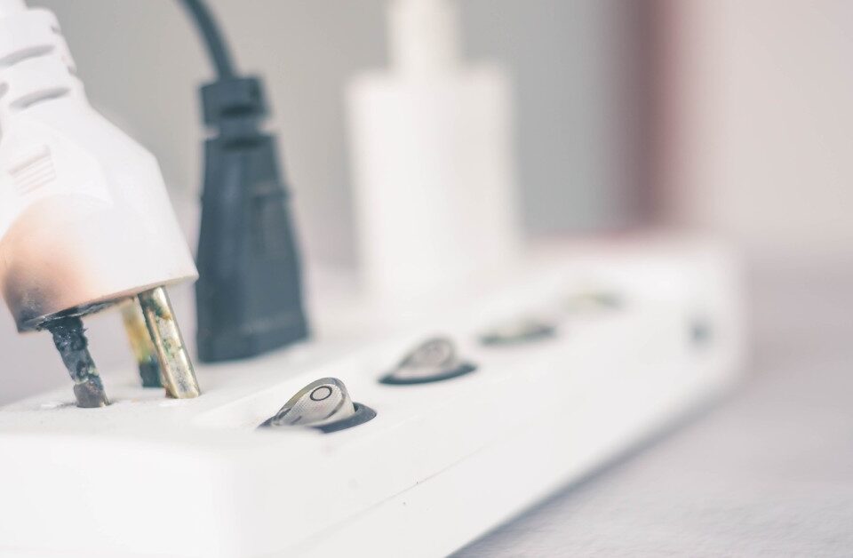 A power strip with three cables plugged into it. The plug in the foreground is noticeably damaged and burnt.