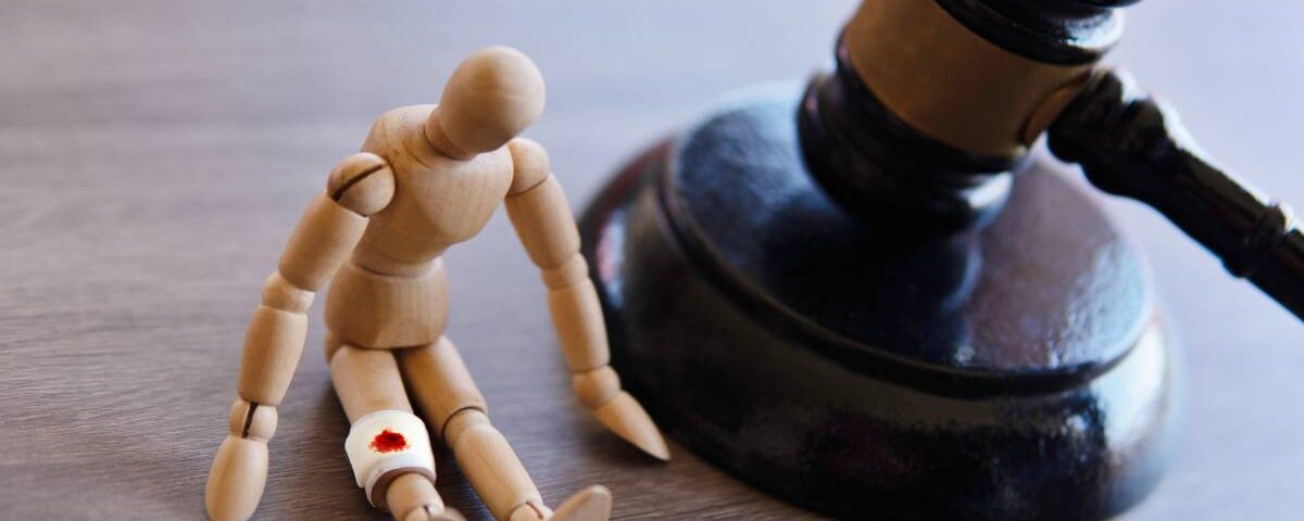 A gavel resting on a table next to a small wooden mannequin that is slumped over and has a gauze bandage around one leg.