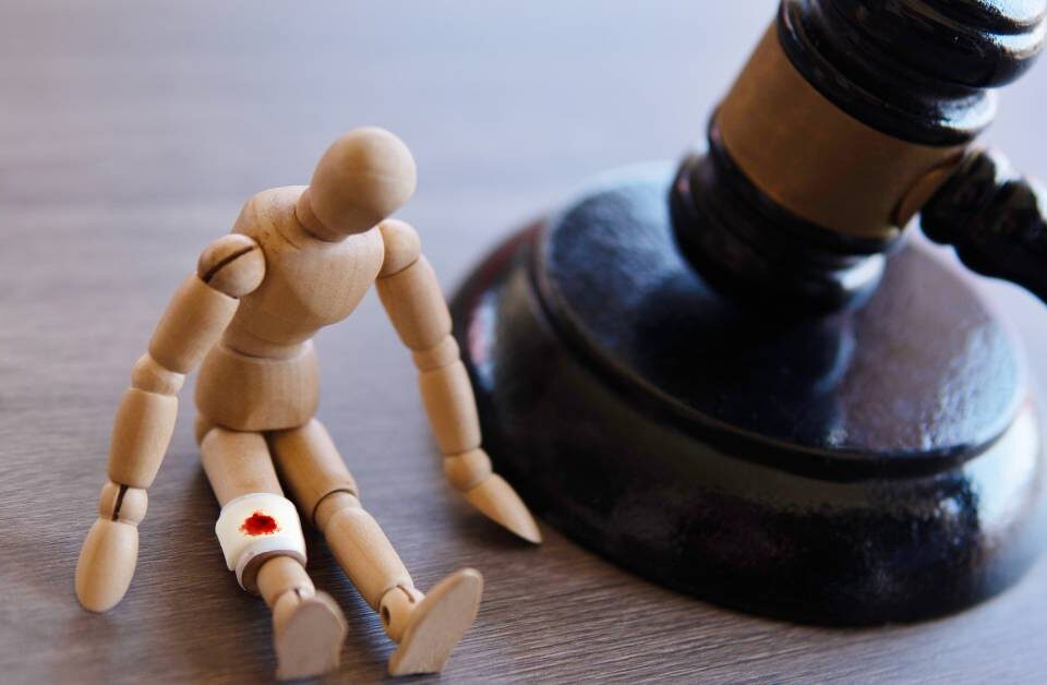 A gavel resting on a table next to a small wooden mannequin that is slumped over and has a gauze bandage around one leg.