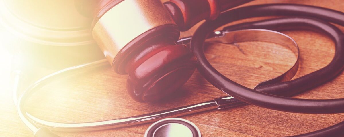 A stethoscope and a wooden gavel placed close together on a table. They are gently lit from the left by natural light.
