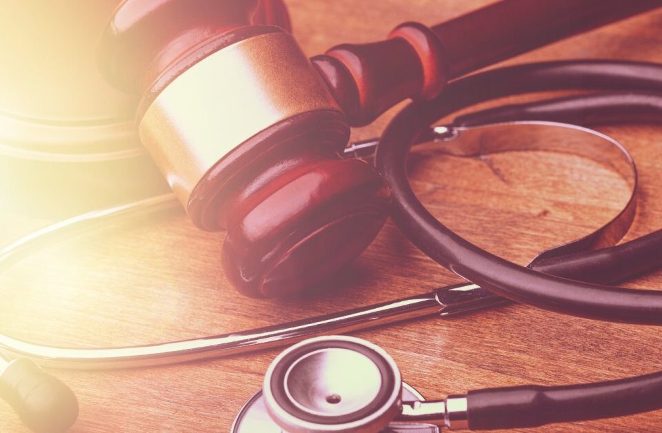 A stethoscope and a wooden gavel placed close together on a table. They are gently lit from the left by natural light.