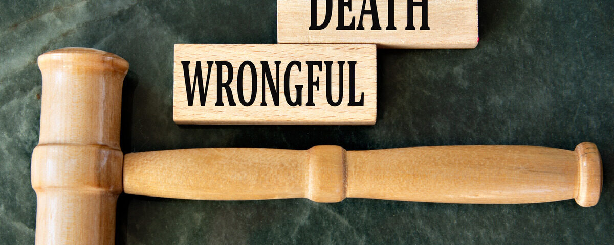 A plain wooden gavel lays horizontally on a marble table. Nearby are two wooden blocks that read “Wrongful” and “Death.”