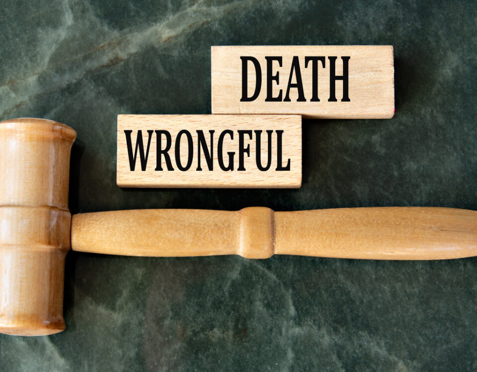 A plain wooden gavel lays horizontally on a marble table. Nearby are two wooden blocks that read “Wrongful” and “Death.”