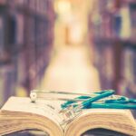 At the end of a library’s aisle, several books sit on a table. One book is open, with a stethoscope laid on top.