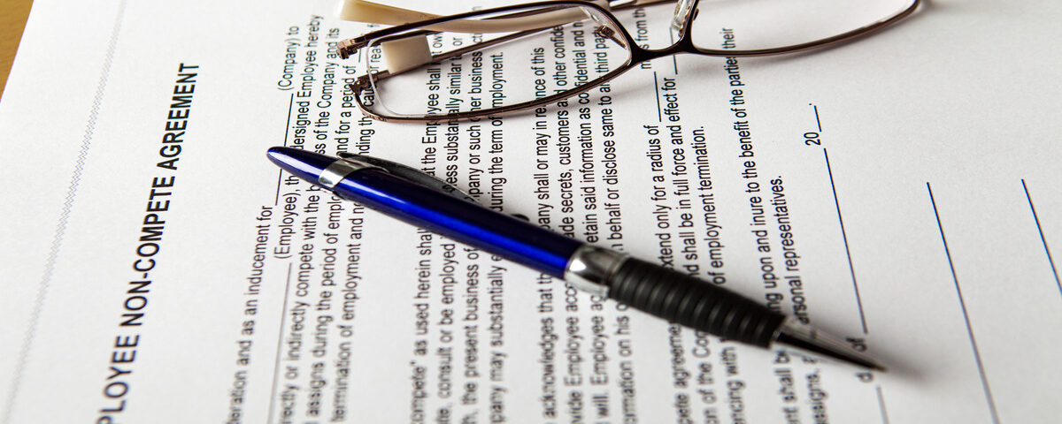 A printed employee non-compete agreement is laid out on a table. A pen and a pair of glasses rest on it.