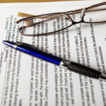 A printed employee non-compete agreement is laid out on a table. A pen and a pair of glasses rest on it.
