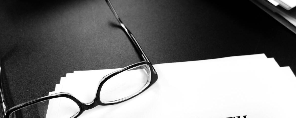 A close-up view shows scattered paper on a black surface with black glasses on top. The top paper reads "Wrongful Death."