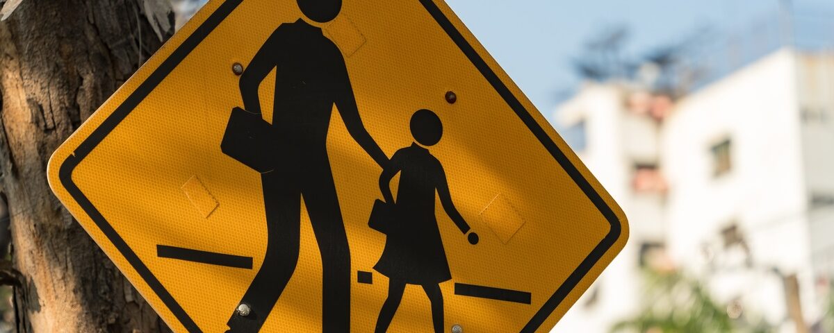 A yellow pedestrian crossing sign that features an adult and child walking across a road.
