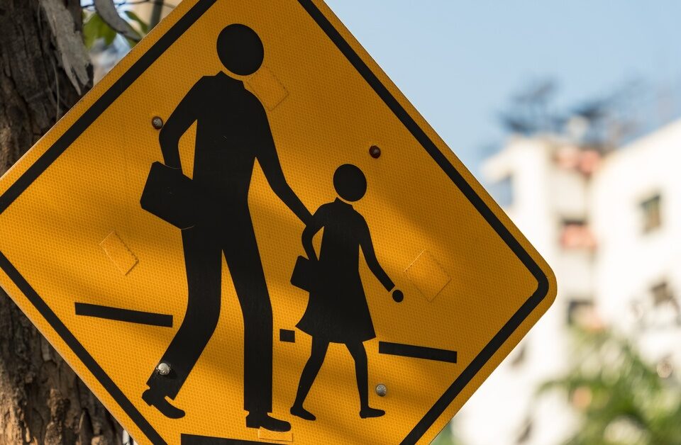 A yellow pedestrian crossing sign that features an adult and child walking across a road.