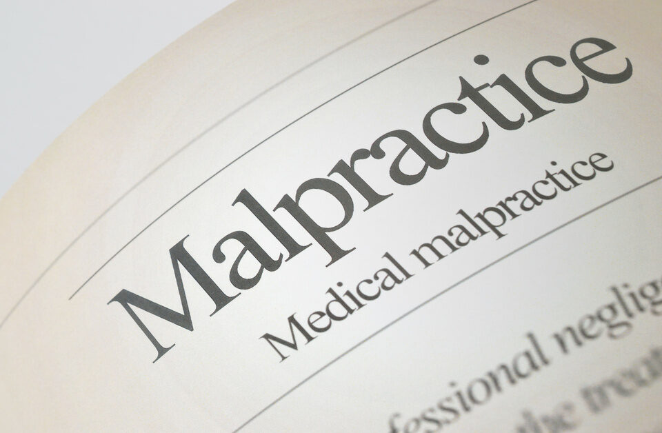 A close-up of a newspaper journal with the title "Malpractice; Medical Malpractice" at the very top.