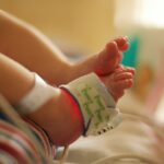 The feet of a newborn baby in a hospital setting. There is a pulse oximeter attached to one of the feet.