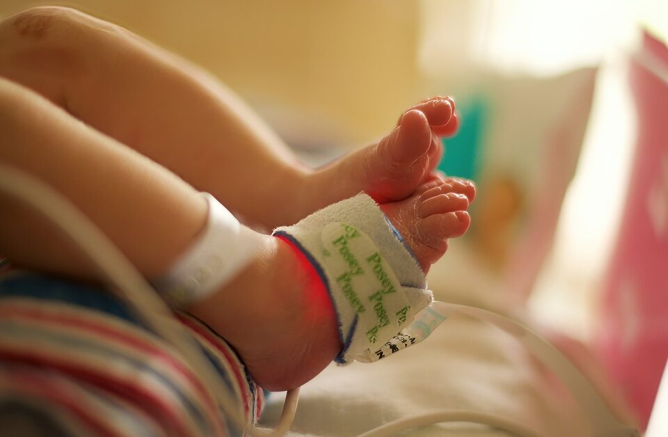 The feet of a newborn baby in a hospital setting. There is a pulse oximeter attached to one of the feet.