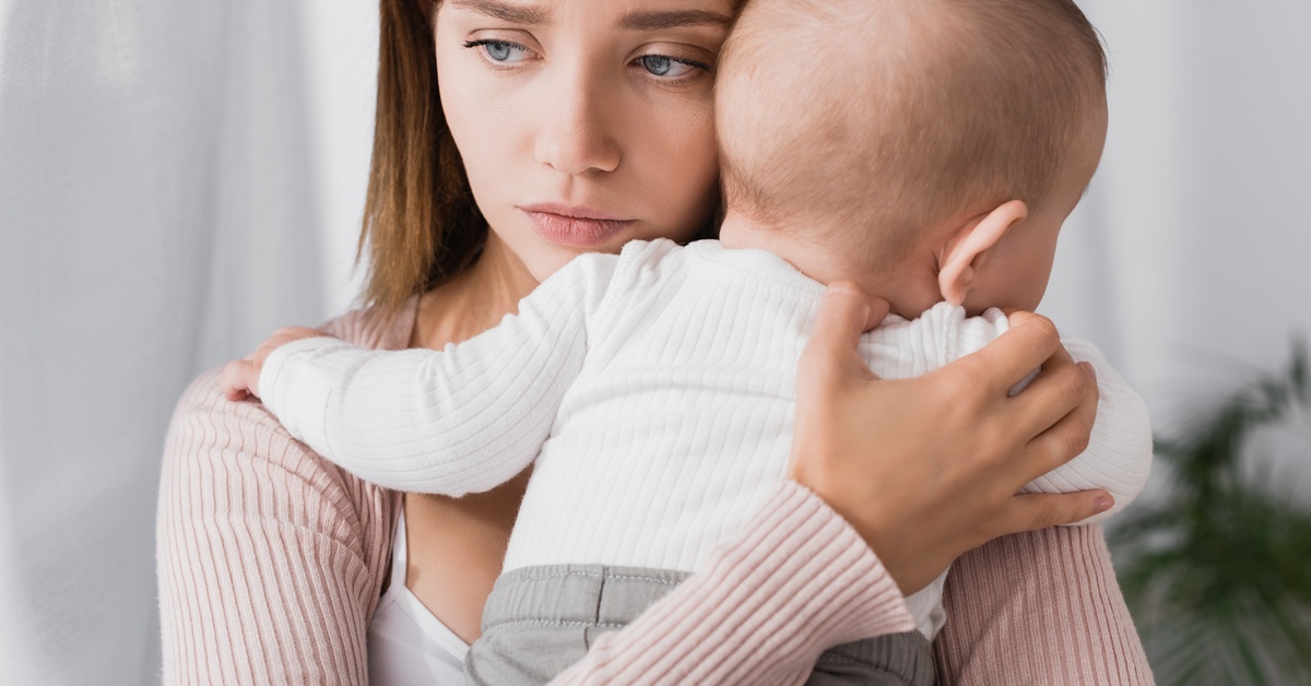 A woman has a worried look on her face while she holds a baby against her chest.