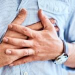 A man experiencing chest discomfort is pressing both of his hands over his heart.