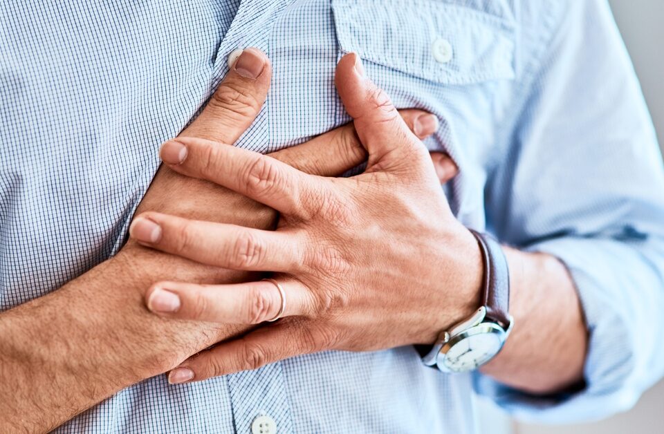 A man experiencing chest discomfort is pressing both of his hands over his heart.