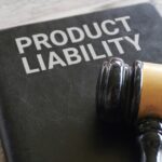 A close-up of a judge gavel resting on top of a black leather folder displaying the words “product liability” on the front.