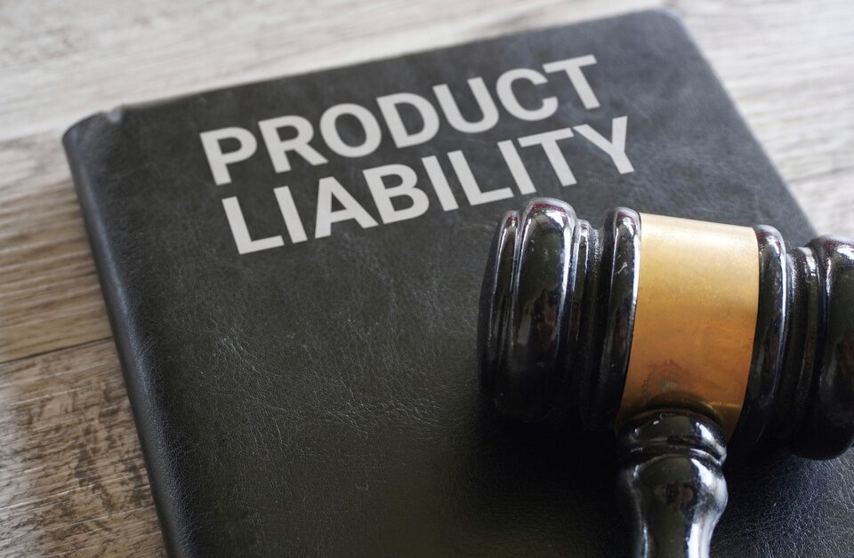 A close-up of a judge gavel resting on top of a black leather folder displaying the words “product liability” on the front.