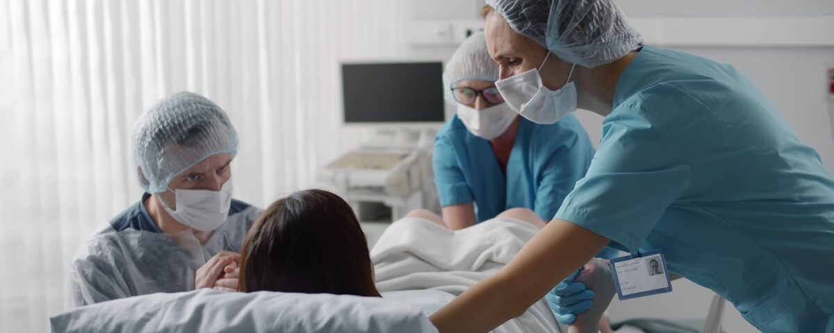 A close-up view shows a baby's hand gently holding the finger of an adult's hand. The background is a white blanket.