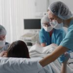 A close-up view shows a baby's hand gently holding the finger of an adult's hand. The background is a white blanket.