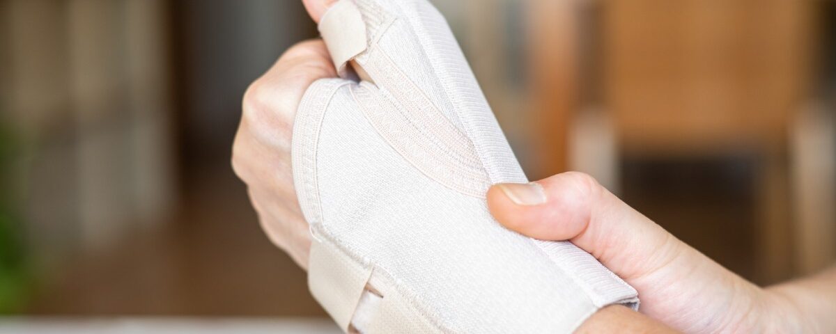 A close-up of a hand wearing an orthopedic brace while holding the wrist with the other hand, with a blurry background.