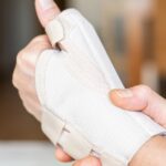 A close-up of a hand wearing an orthopedic brace while holding the wrist with the other hand, with a blurry background.