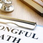 A close-up of a clipboard with a piece of paper displaying the words “wrongful death” next to a stethoscope and a book.
