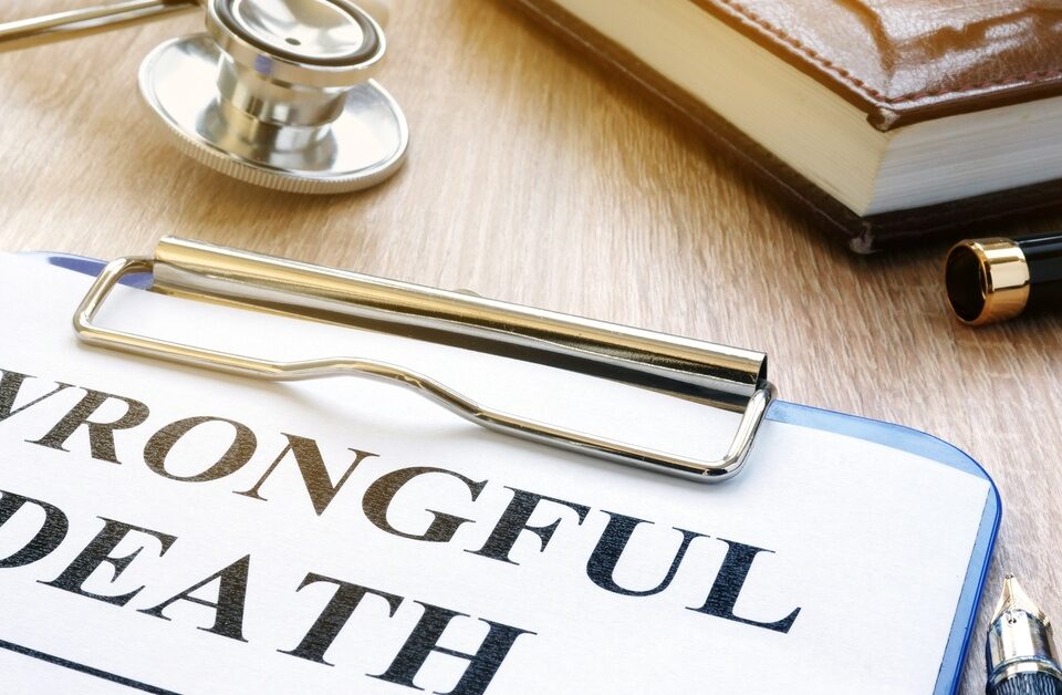 A close-up of a clipboard with a piece of paper displaying the words “wrongful death” next to a stethoscope and a book.