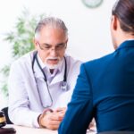 A man wearing a blue suit, sitting across from a man wearing a white robe behind a desk with a wooden gavel on top.