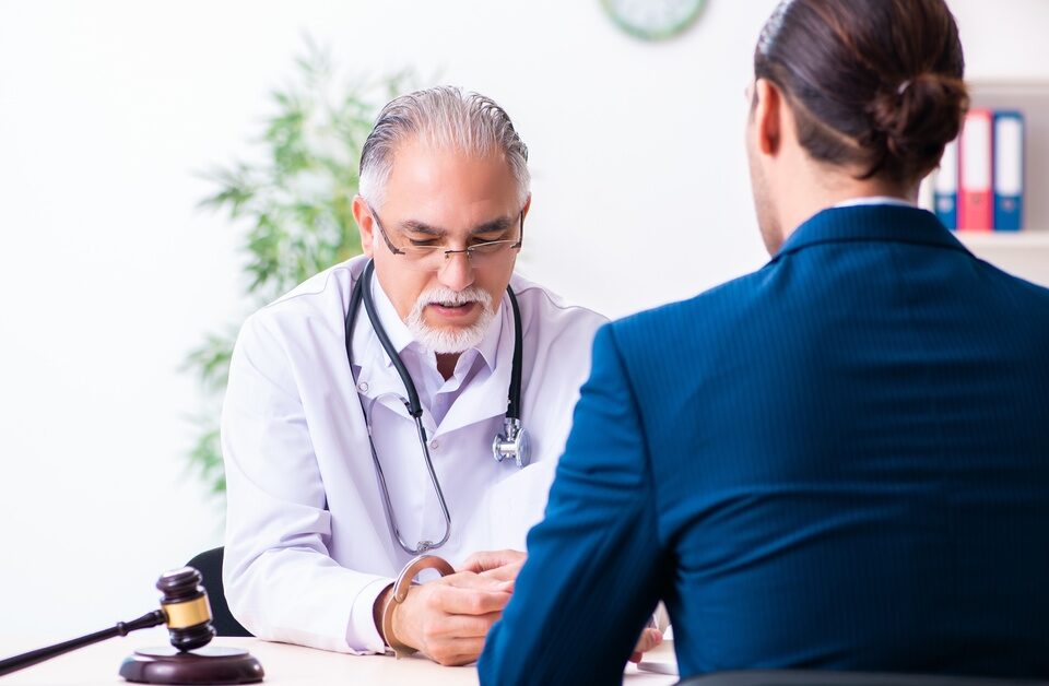 A man wearing a blue suit, sitting across from a man wearing a white robe behind a desk with a wooden gavel on top.